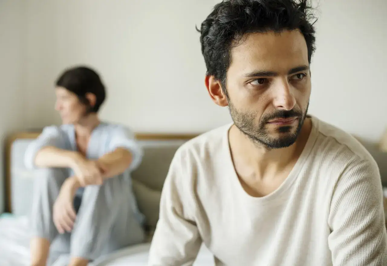 Uomo pensieroso, con una donna sfocata sullo sfondo. La loro relazione è complessa, un amore che affronta le sfide di una persona bipolare.