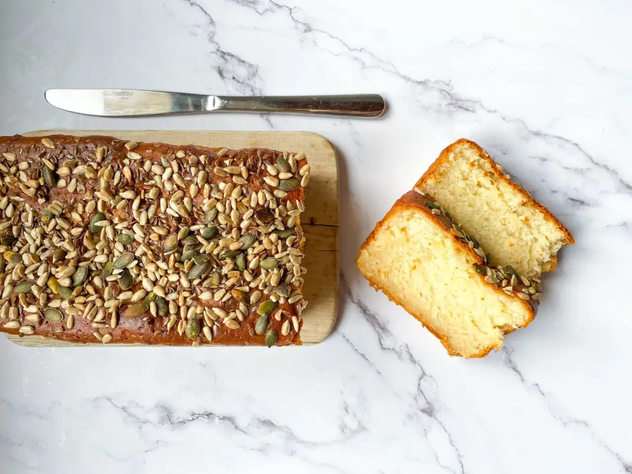 Plumcake senza uova, soffice e dorato, ricoperto di semi misti. Due fette tagliate mostrano la sua morbidezza.