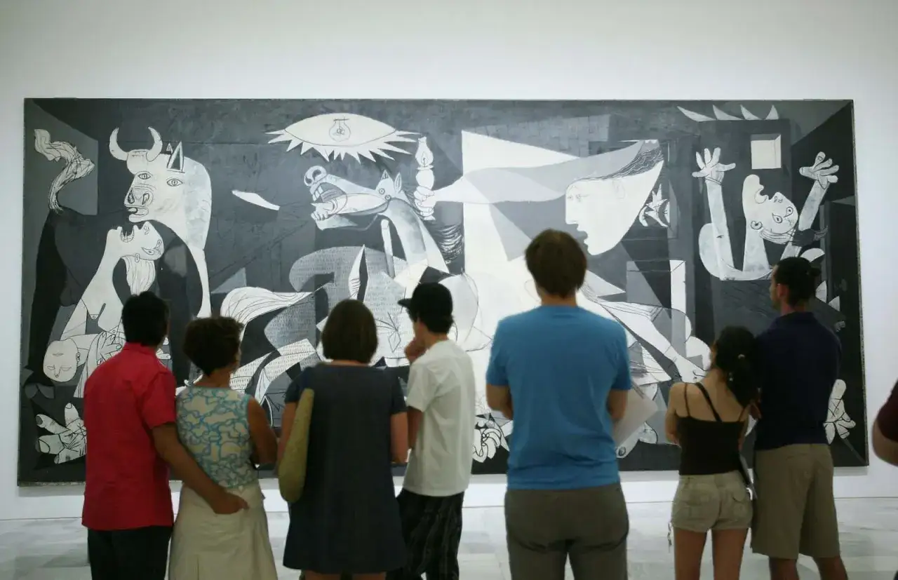 Ludzie podziwiają Guernicę, jedno z najsłynniejszych obrazów Pablo Picasso. Monumentalne dzieło w czerni i bieli ukazuje cierpienie wojny.