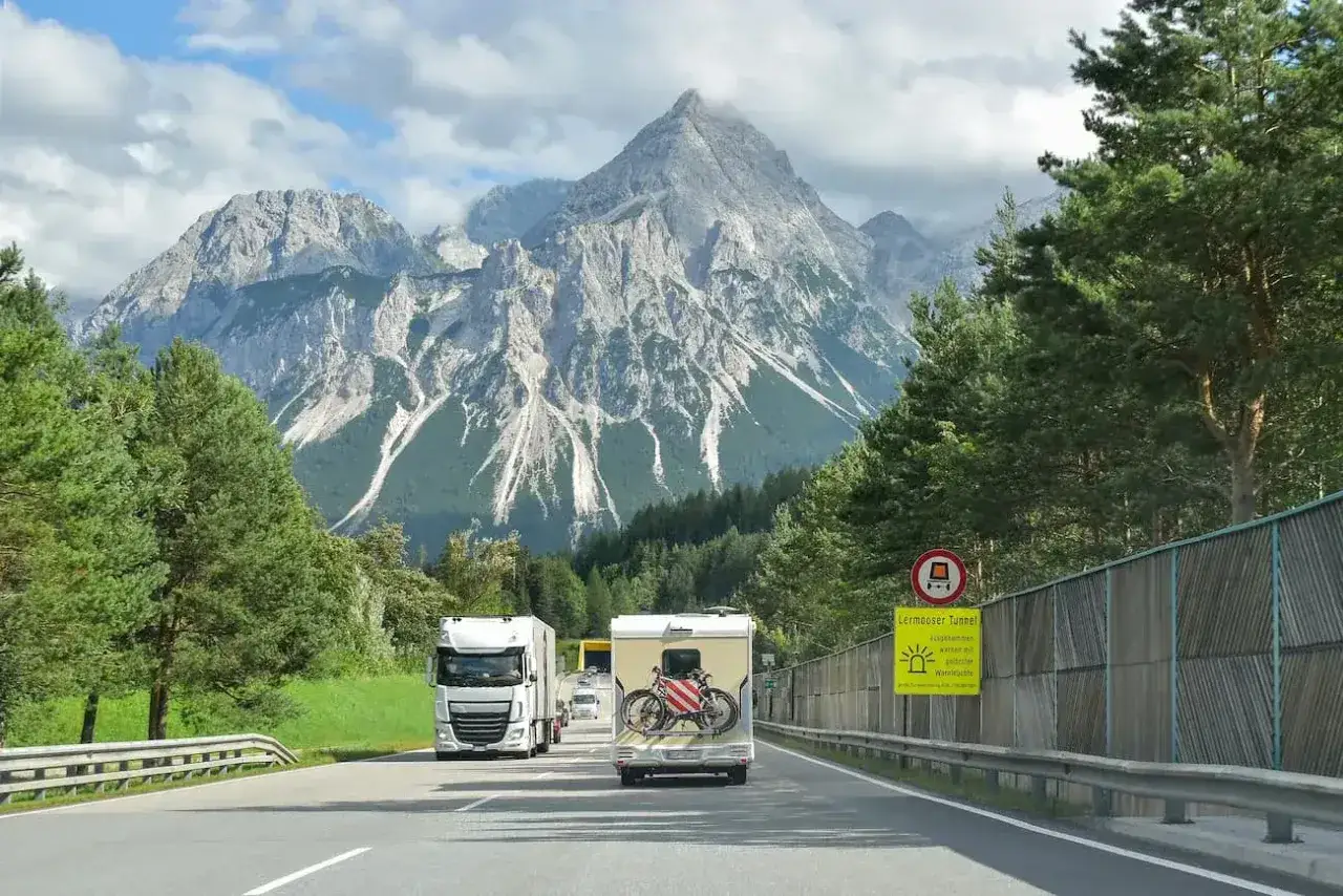 Ciężarówka i kamper jadą drogą w Austrii. Znak informuje o opłatach drogowych Austria powyżej 3,5 tony.