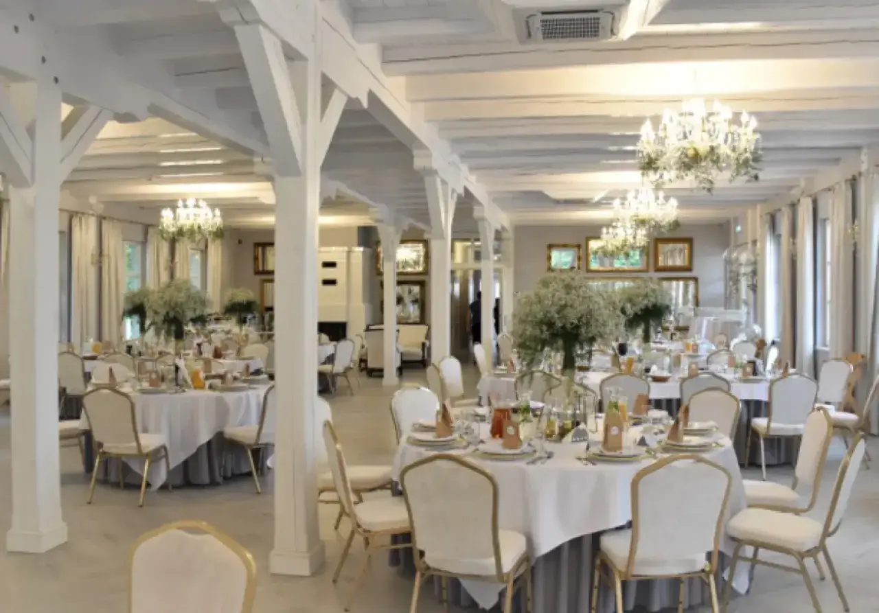 Elegancka sala bankietowa dworu pod kasztanowcami, udekorowana białymi obrusami, kwiatami i kryształowymi żyrandolami, gotowa na przyjęcie gości.