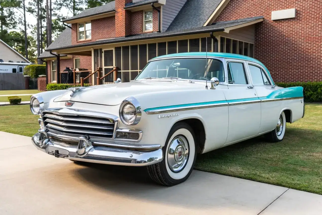 En vit och turkos Chrysler 58 parkerad framför ett tegelhus. Klassisk amerikansk bil med kromdetaljer.