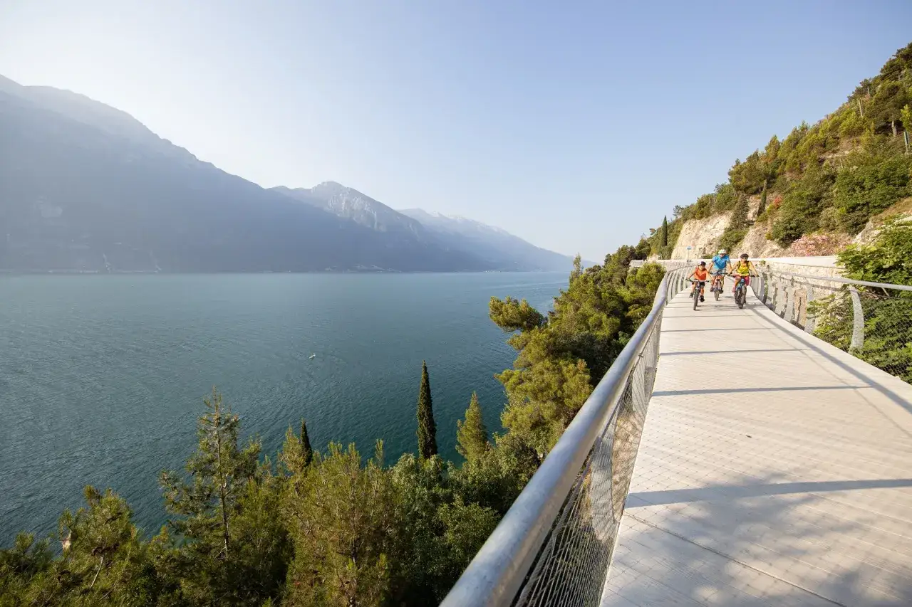 Famiglia in bici sulla ciclovia del Garda, con vista mozzafiato sul lago e le montagne.