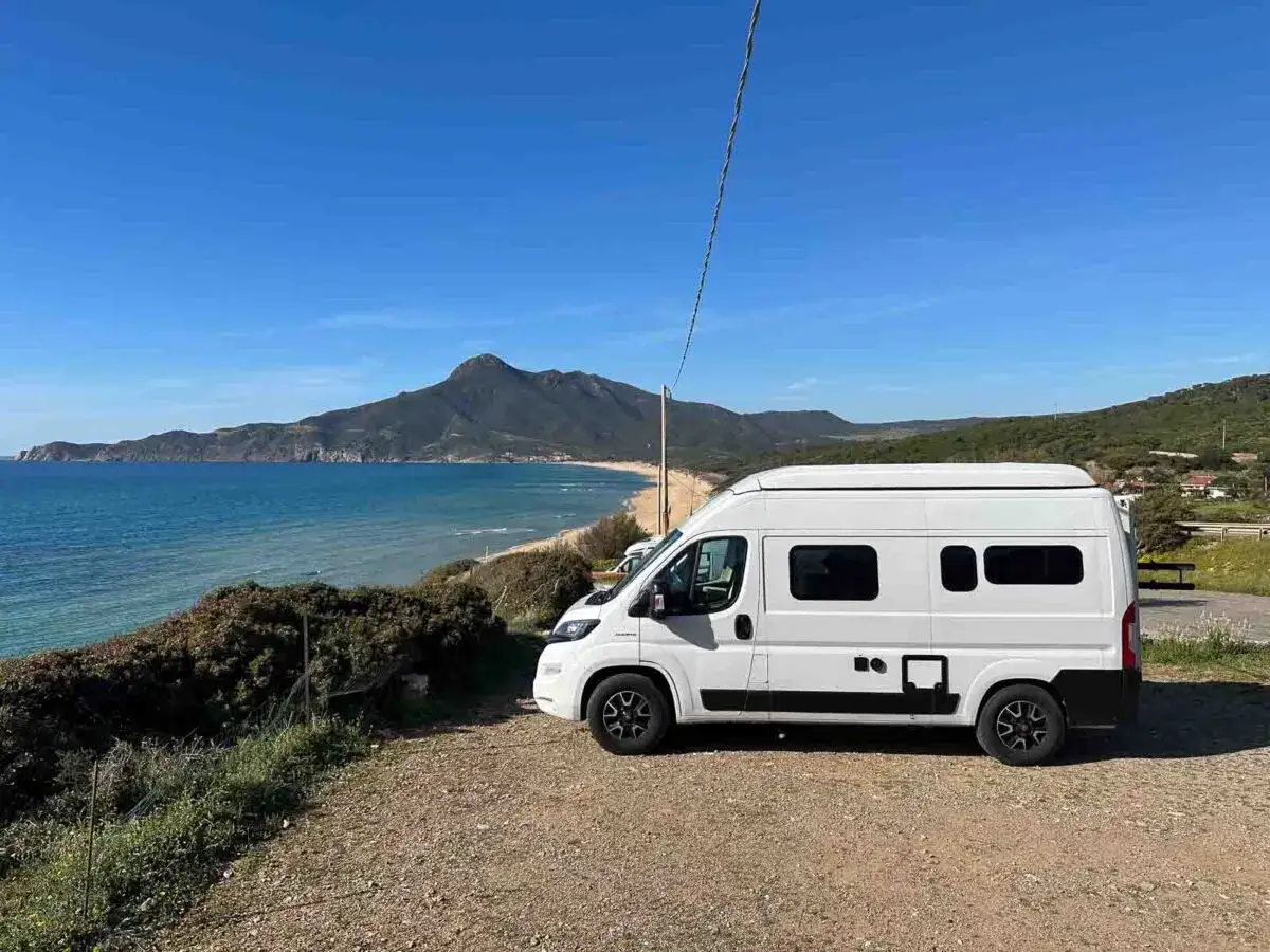 Ein weißer Camper steht an der Küste Sardiniens. Die Landschaft mit Bergen und Meer deutet auf die beste Reisezeit Sardinien hin.