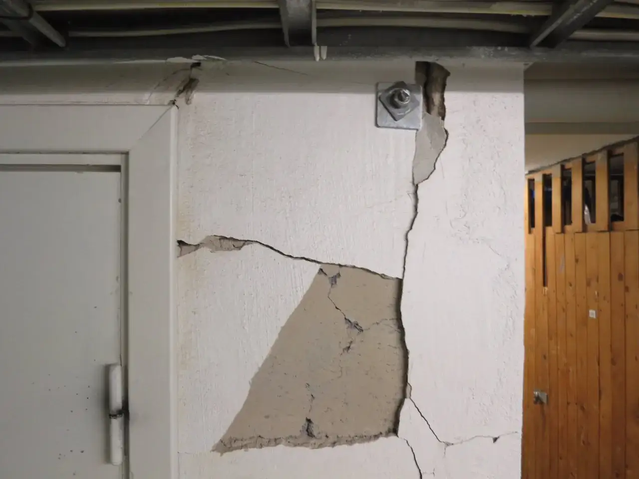 Stora sprickor i en vit v&auml;gg, en d&ouml;rr till v&auml;nster. Behov av att laga sprickor i grunden.
