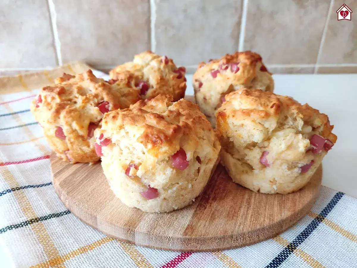 Cinque muffin salati morbidissimi con cubetti di prosciutto rosa, su un tagliere di legno, pronti per essere gustati.
