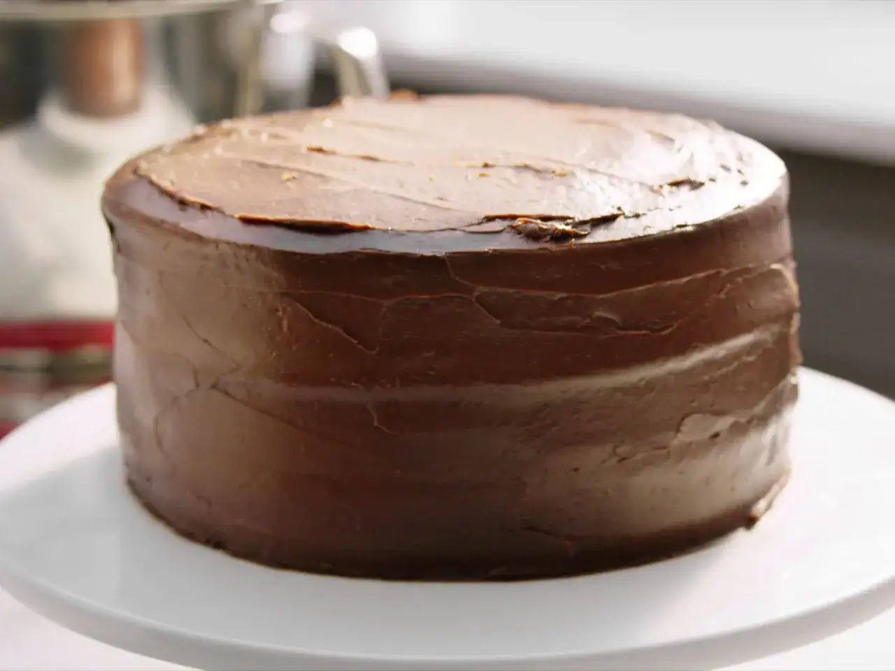 Eine k&ouml;stliche, runde Schoko Torte mit dunkler Schokoladenglasur, die auf einem wei&szlig;en Tortenst&auml;nder steht.