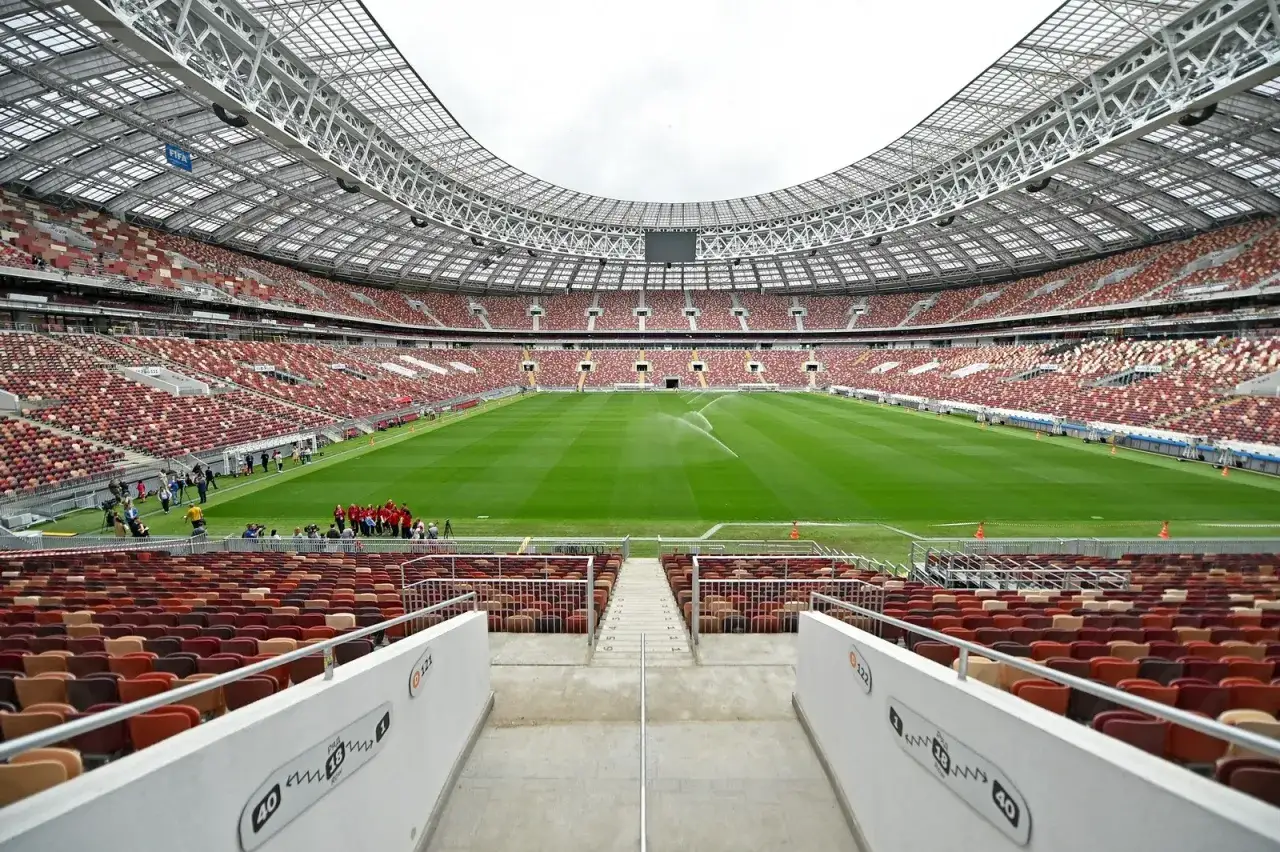 Pusta, nowoczesna arena piłkarska z rzędami czerwono-brązowych siedzeń, gotowa na mecze klubów piłkarskich z Moskwy.