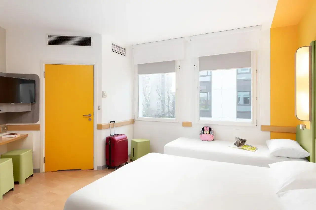 Pokój w ibis budget warszawa centrum: dwa łóżka, żółte drzwi, czerwona walizka, plecak Myszki Miki.