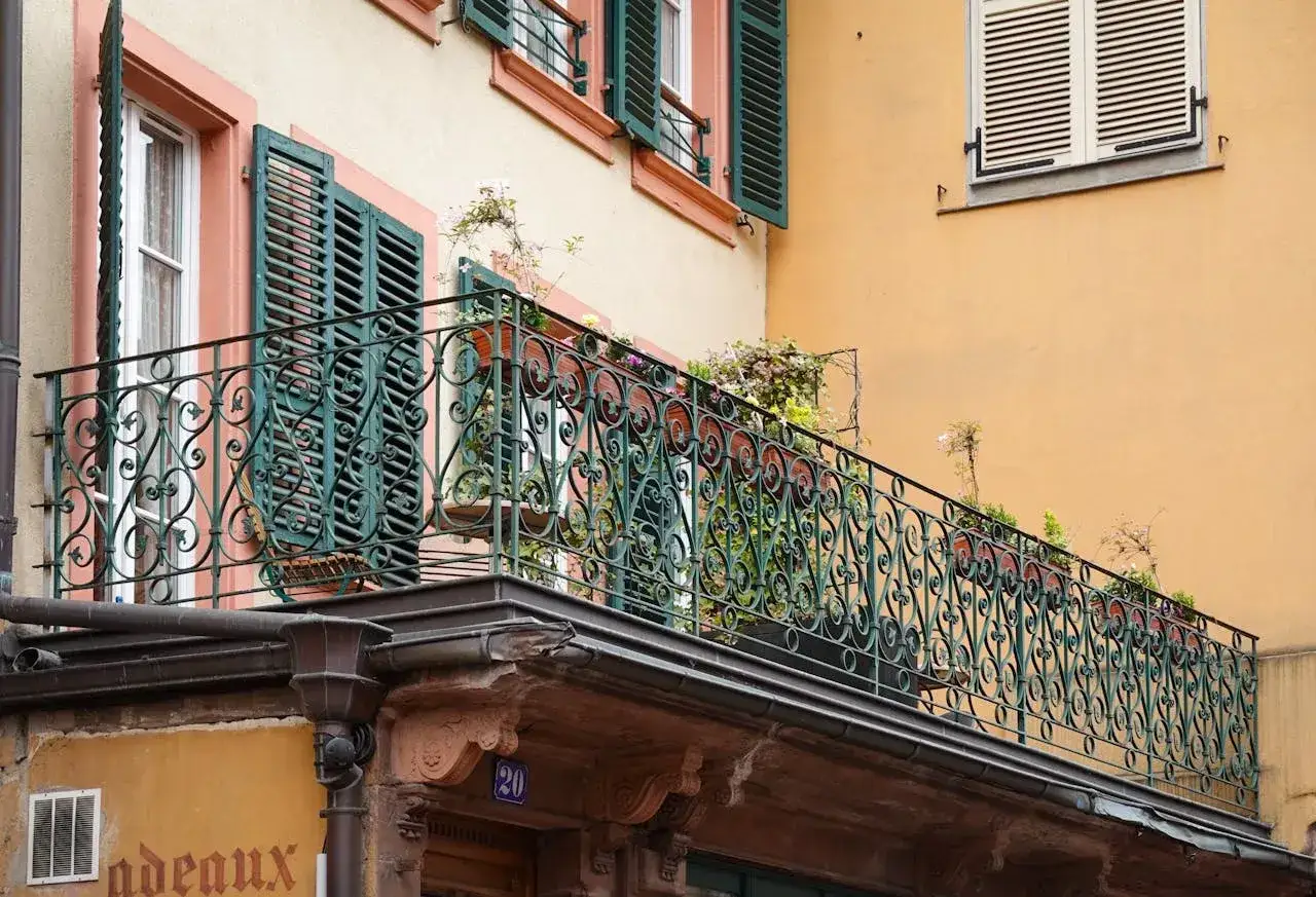 Kuty balkon z kutą balustradą i roślinami. Czy balkon jest częścią wspólną? Trudno ocenić po zdjęciu.