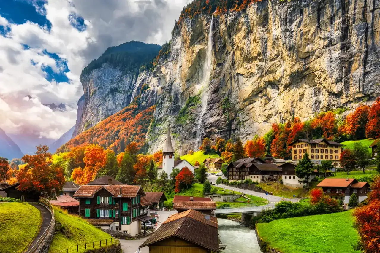 Un pintoresco pueblo suizo que ver en otoño, con casas de madera, una iglesia y cascadas cayendo por acantilados imponentes.