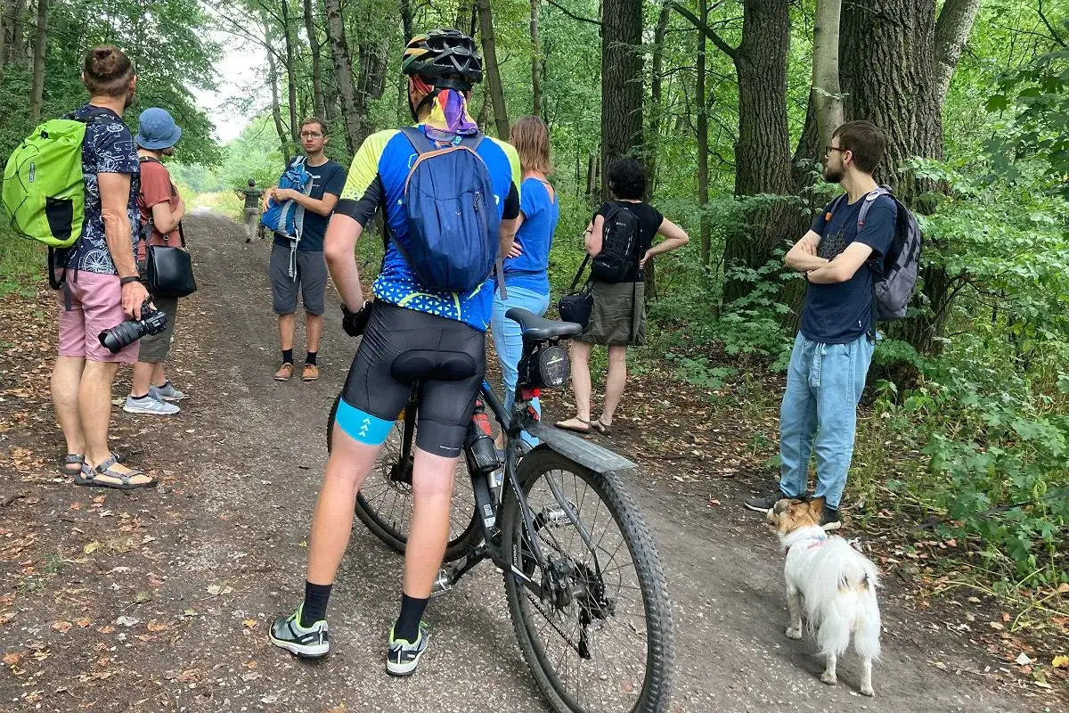 Grupa ludzi z rowerami i psem na leśnej ścieżce. Wszyscy ubrani są w sportowe stroje, gotowi na wycieczkę po **wartostradzie Poznań**.