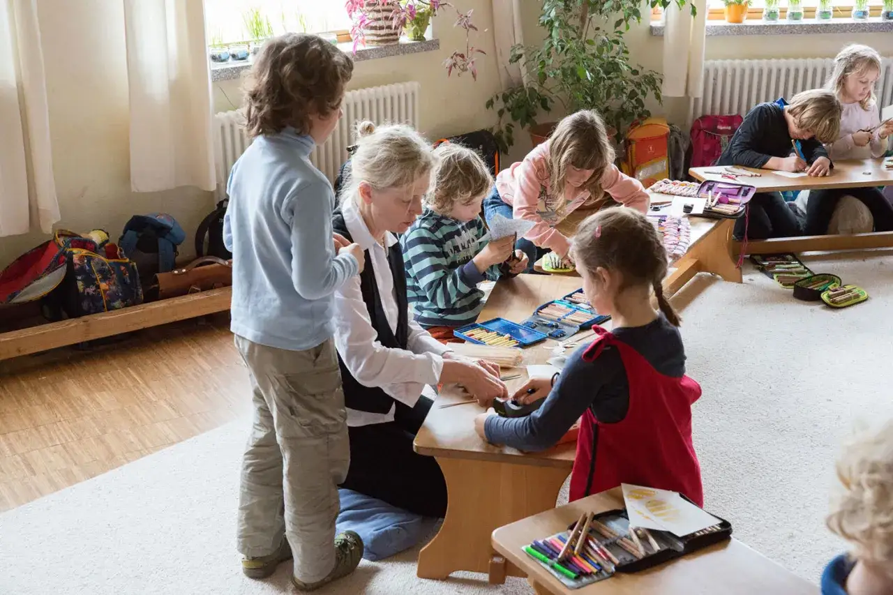 Kinder und Lehrerin basteln und malen. Kreatives **lernen in bewegung** mit Stiften und Papier.