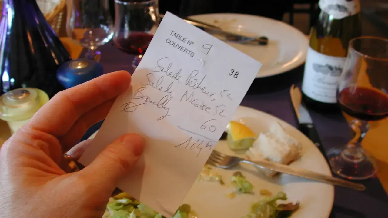 Hand hält Rechnung mit Speisen und Preisen. Nach dem Essen in Holland überlegt man, wie viel Trinkgeld angemessen ist.