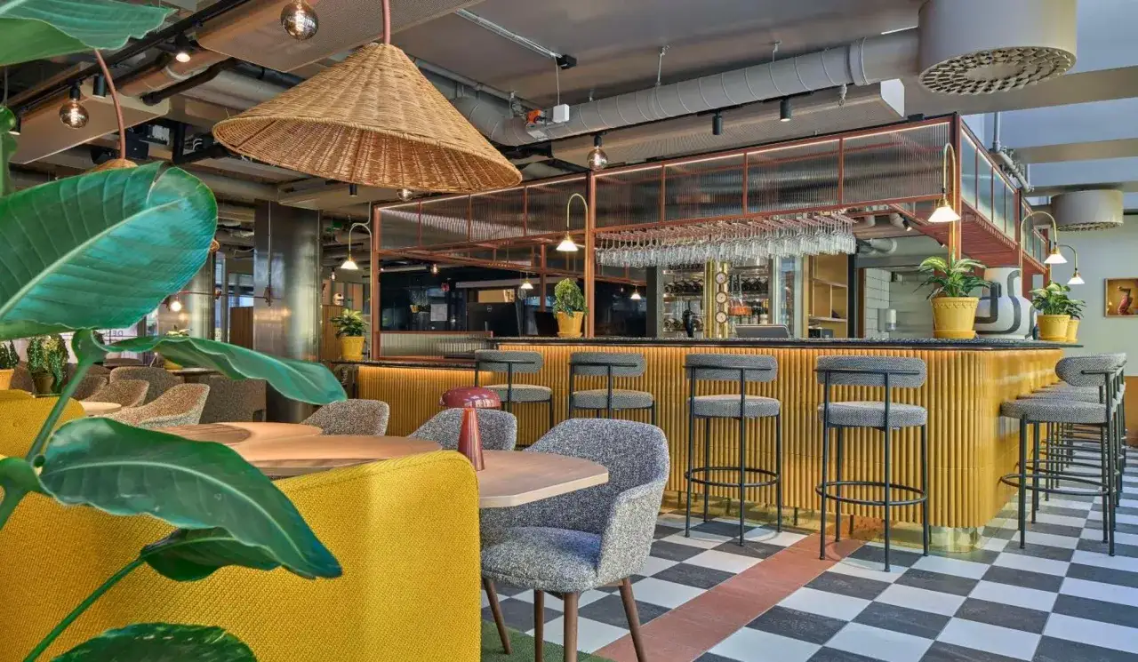 En modern bar med gula detaljer och rutigt golv. Perfekt f&ouml;r en drink p&aring; restauranger norra Bantorget.