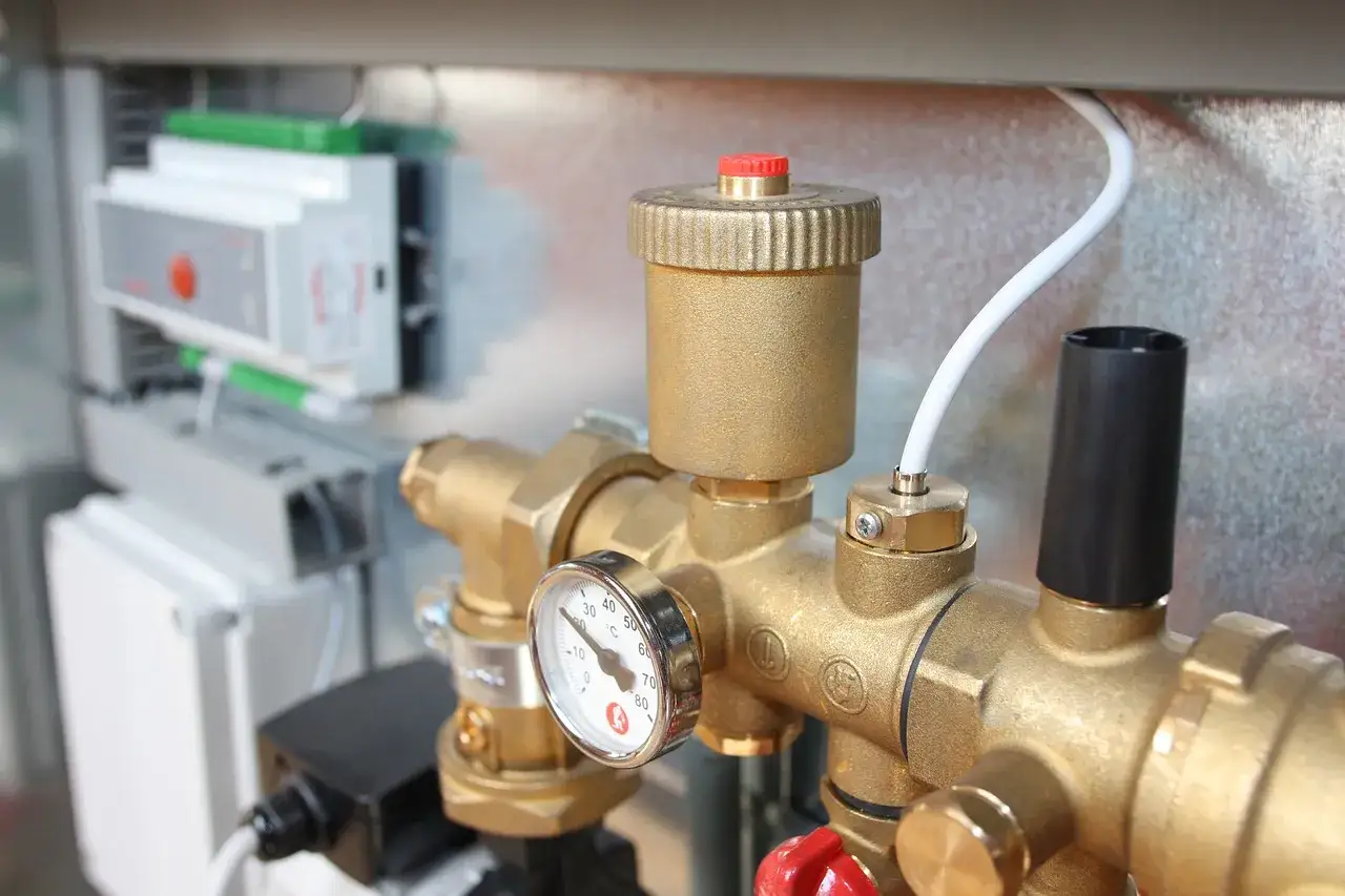 Detalle de tuberías de latón con manómetro y una válvula de seguridad. En el fondo, un panel de control eléctrico.