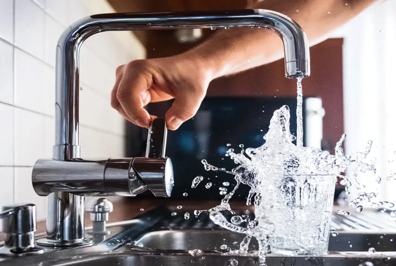 Mano girando la llave para cuidar el agua, que salpica al llenar un vaso.