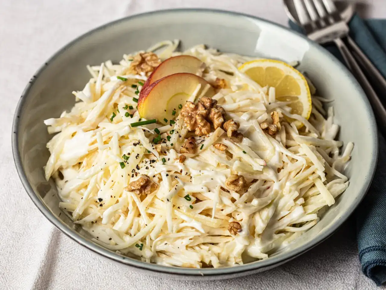 Ein cremiger Selleriesalat mit &Auml;pfeln, Waln&uuml;ssen und einem Zitronenschnitz, garniert mit Schnittlauch und Pfeffer.
