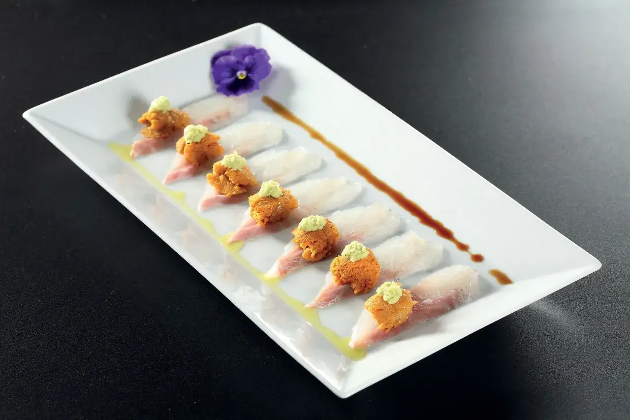 Delizioso sashimi con ricci di mare freschi, guarnito con un fiore viola e salsa.