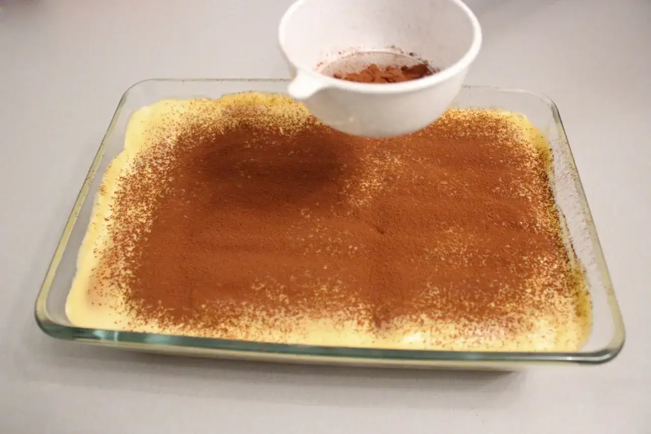 Kakao wird &uuml;ber eine cremige Schicht gestreut, die aus Mascarpone und Eigelb hergestellt wurde.