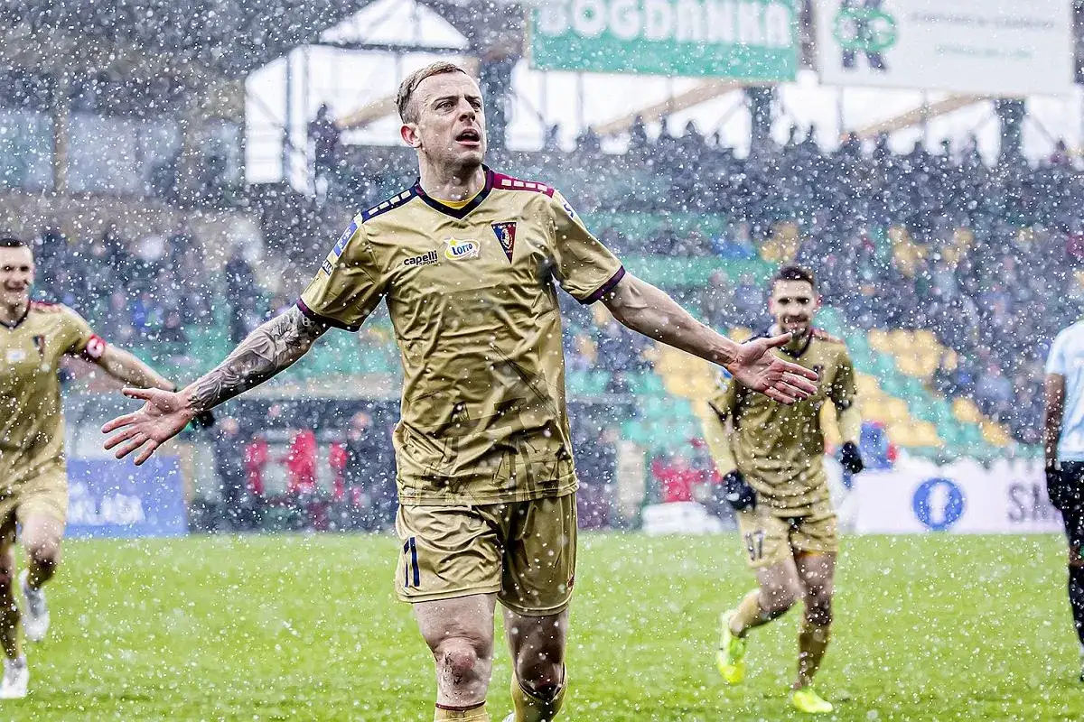 Piłkarz w złotej koszulce, gdzie gra Grosicki, cieszy się na boisku podczas opadów śniegu.