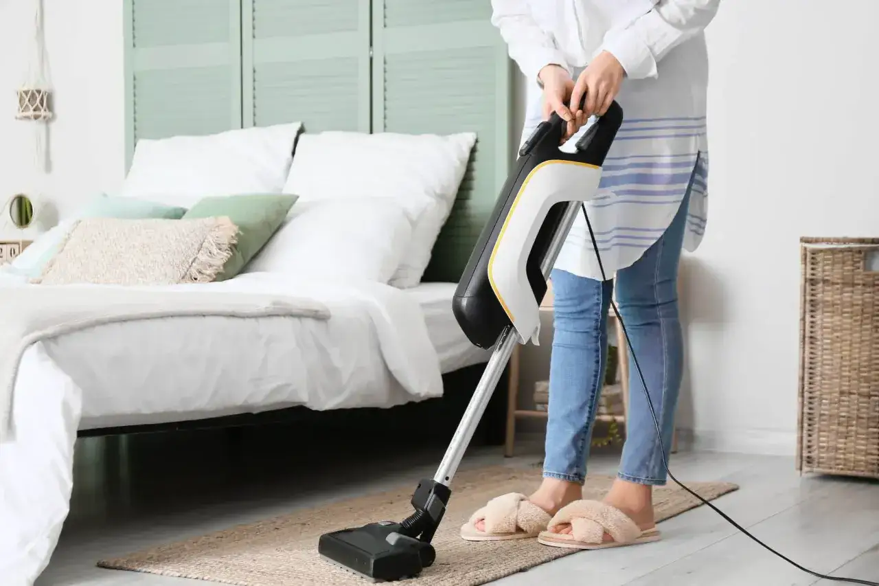Eine Person saugt mit einem modernen Staubsauger den Teppich im Schlafzimmer.