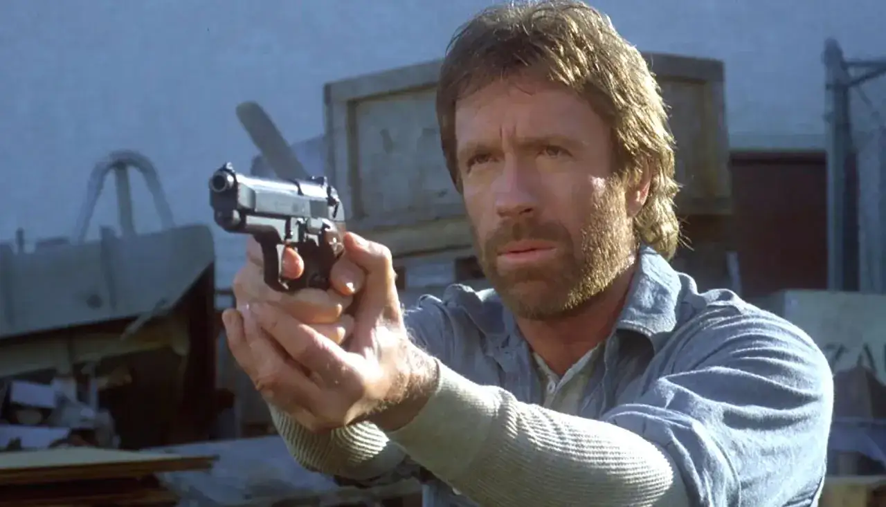 Chuck Norris z pistoletem w ręku, gotowy do akcji w jednym ze swoich kultowych filmów.