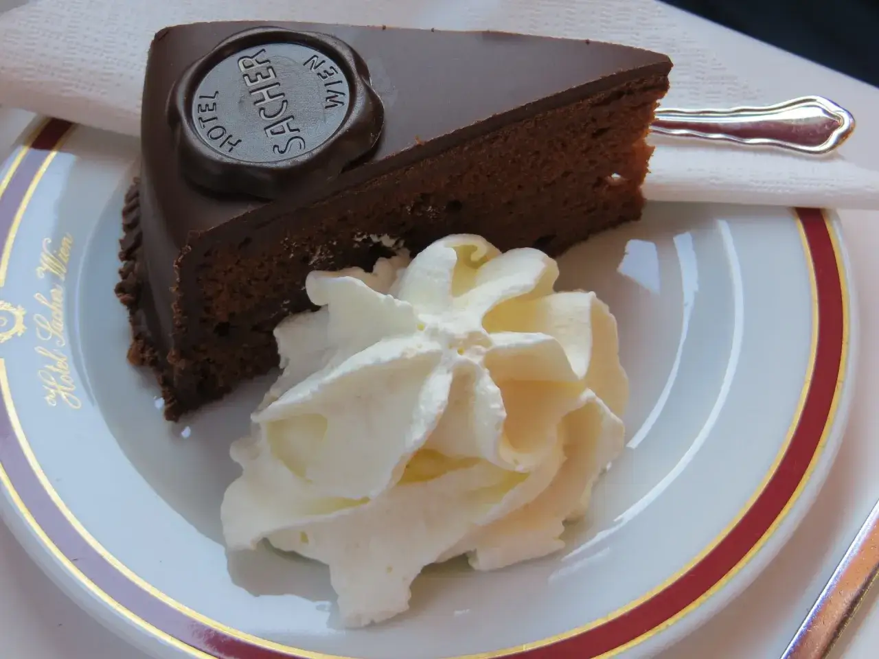 Una fetta di torta viennese Sacher, con panna montata e il logo dell'Hotel Sacher Wien.