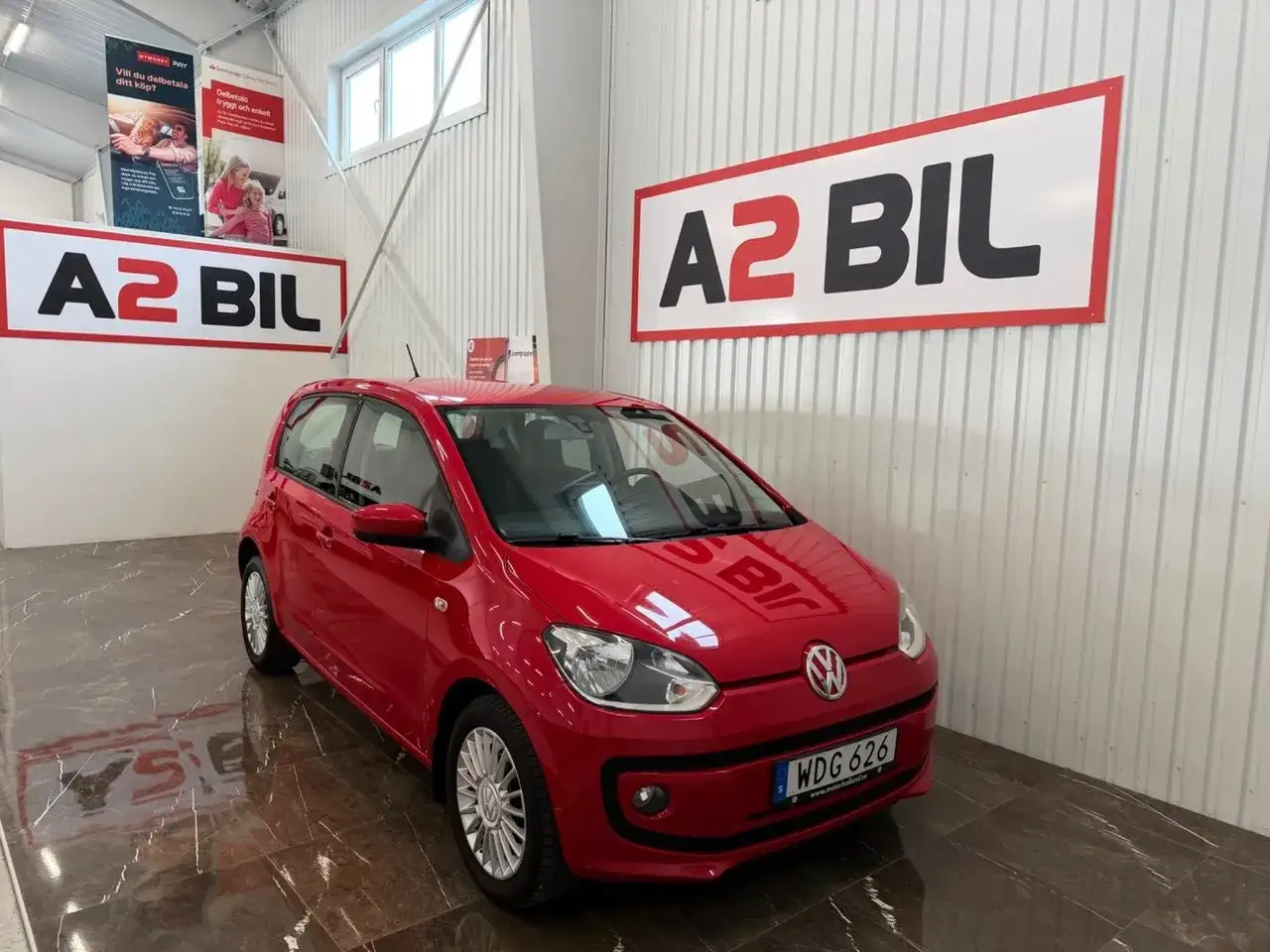 Röd VW Up! står i ett garage. En skylt med