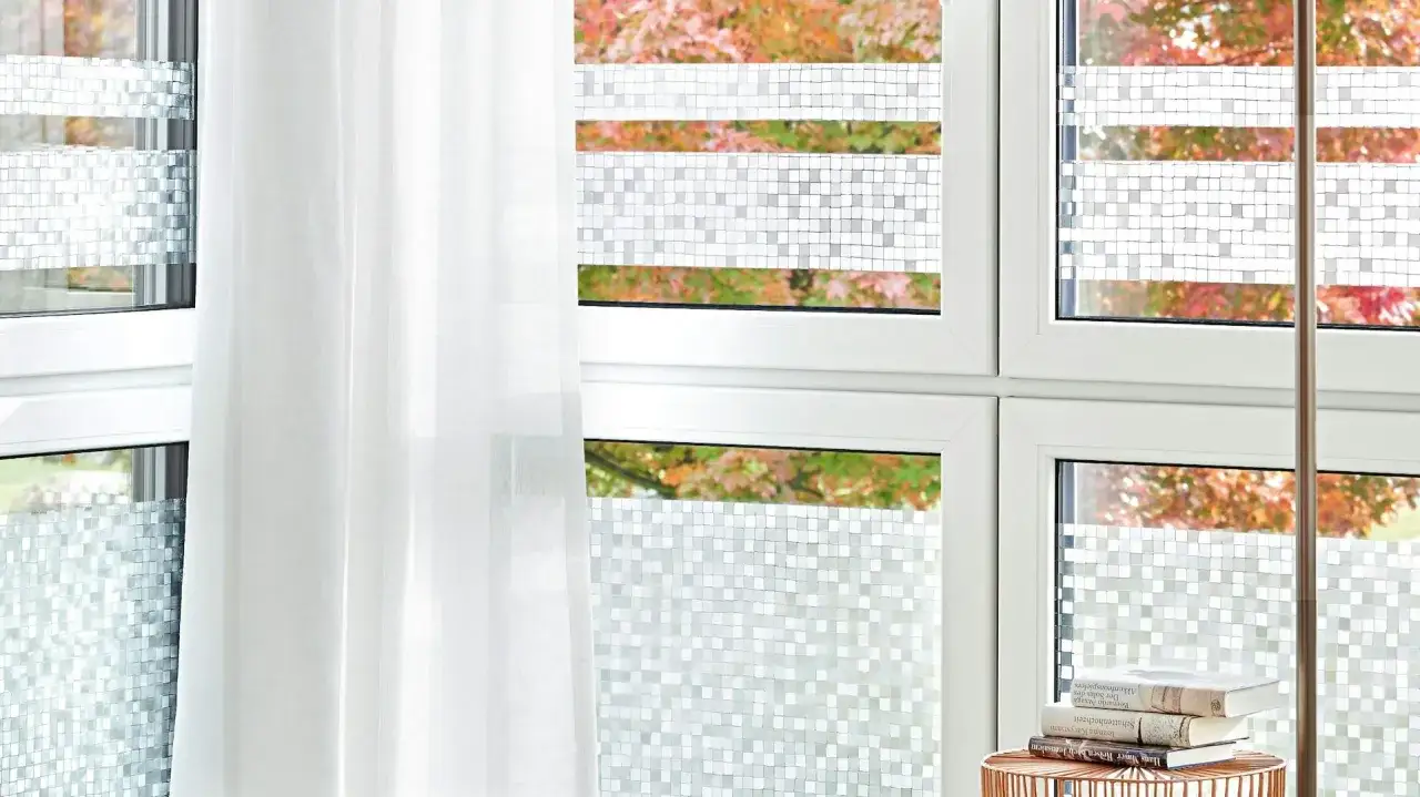 Fenster mit statischer Fensterfolie im Mosaikmuster, die Privatsph&auml;re schafft und das Licht filtert. Ein wei&szlig;er Vorhang h&auml;ngt daneben.