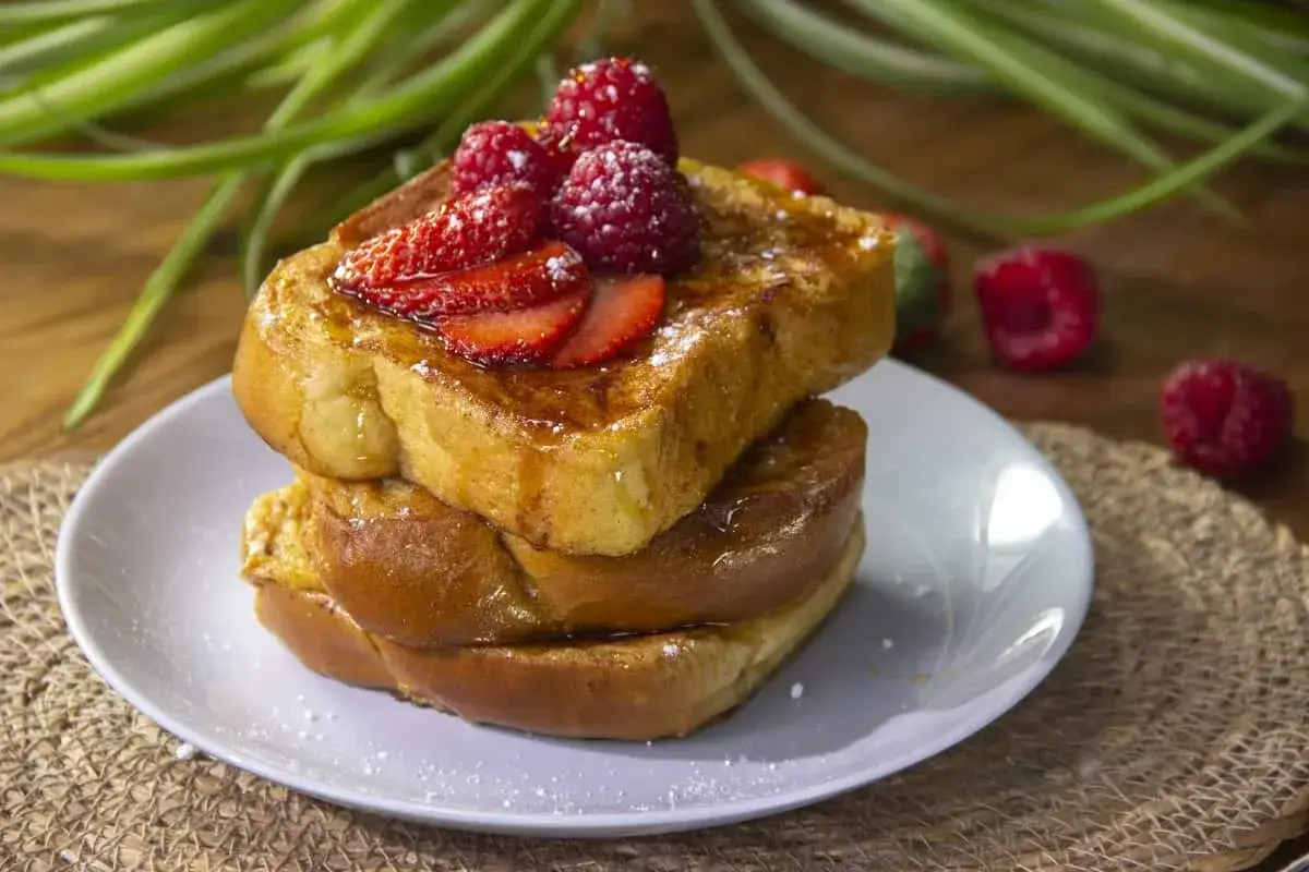 Tostadas francesas doradas y esponjosas, apiladas y cubiertas con fresas, frambuesas y un toque de az&uacute;car glas.