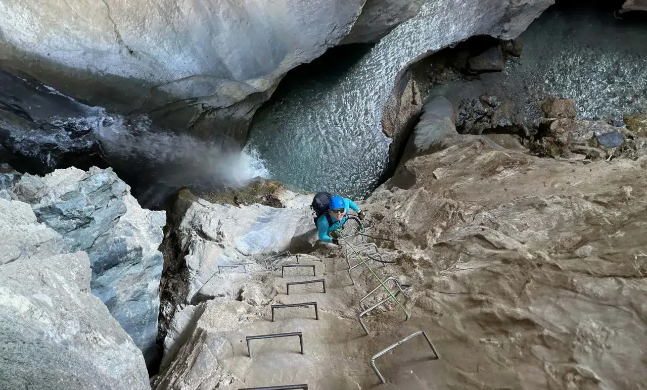 Persona su una scala metallica in una gola, affronta le **ferrate Val di Susa** con una cascata e acqua cristallina.