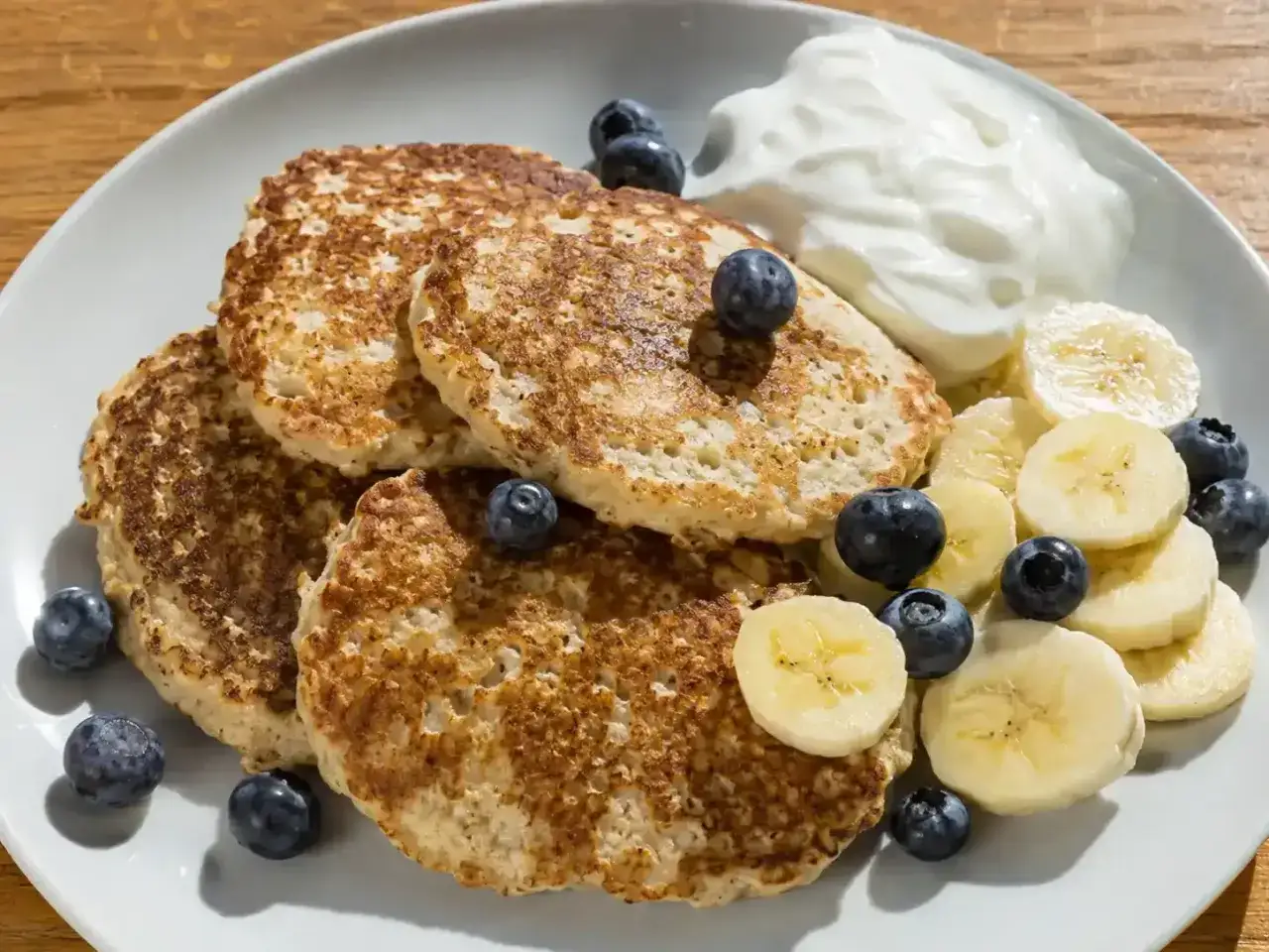 En tallrik med fluffiga bananpannkakor, toppade med blåbär och bananskivor. Serveras med en klick yoghurt. Ett enkelt bananpannkaka recept för en god frukost.