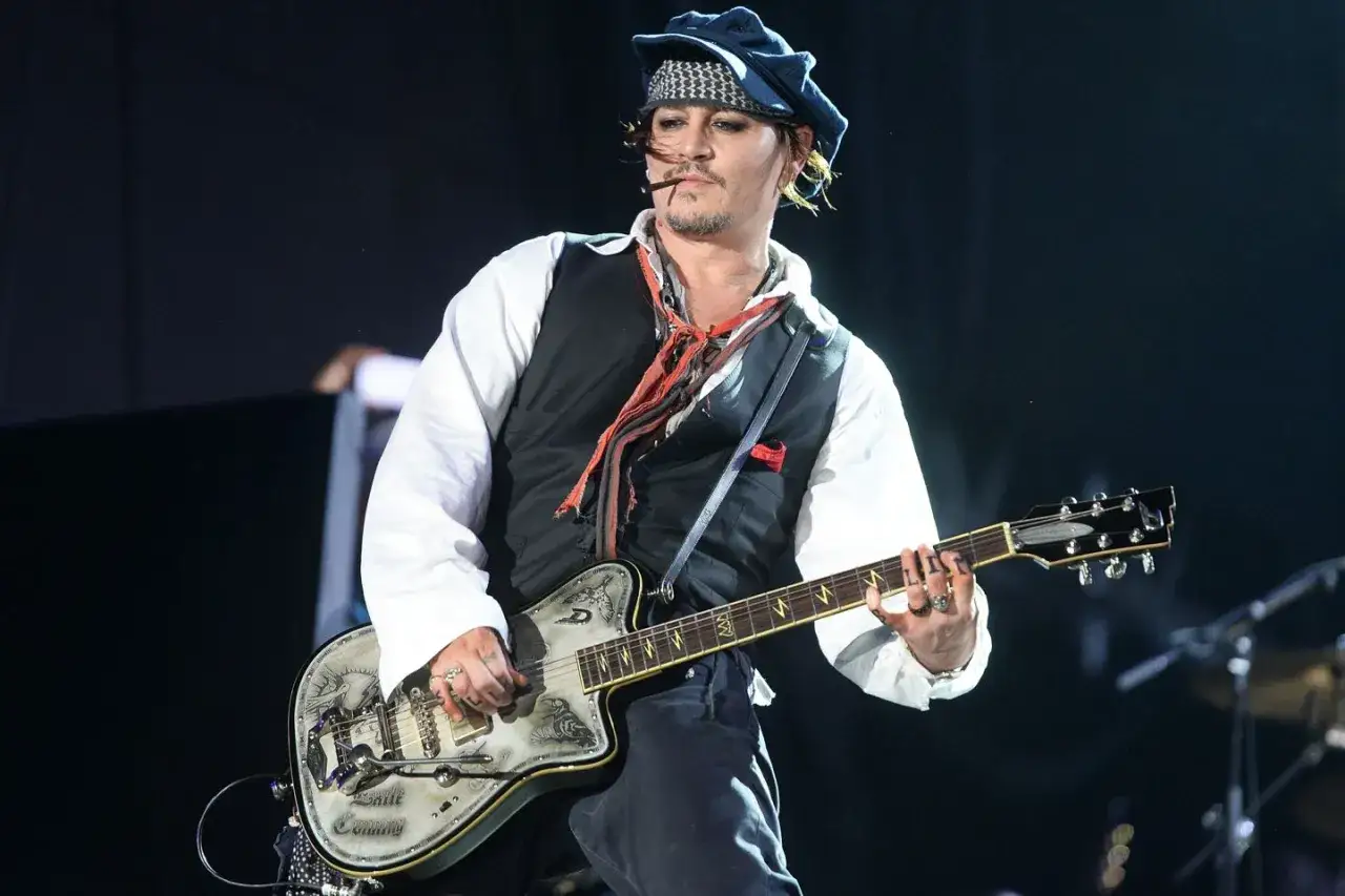 Johnny Depp z zespołem na scenie, grający na ozdobnej gitarze.