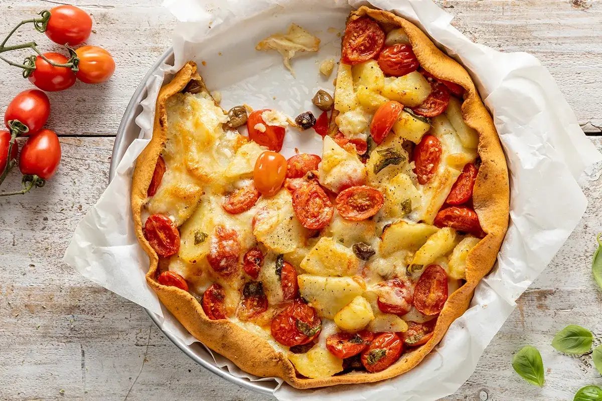 Torta salata con patate e pomodorini, dorata e invitante, con formaggio filante e un contorno di pomodorini freschi.