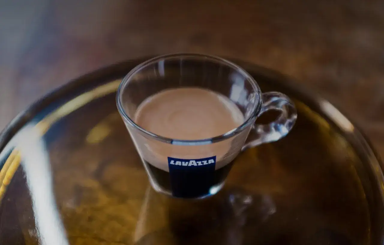 Un bicchiere di vetro con il miglior caffè Lavazza, con la sua crema densa e invitante, su un vassoio dorato.
