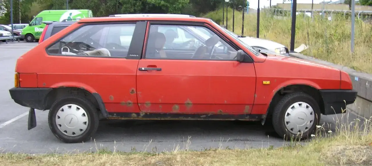 R&ouml;d Lada Samara med rostfl&auml;ckar p&aring; sidan, parkerad utomhus.