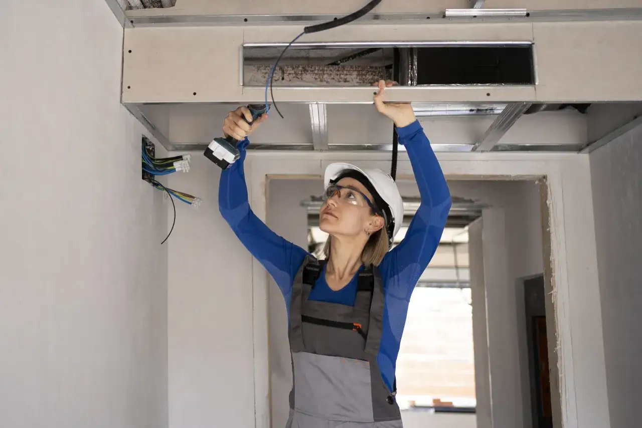 Instaladora trabajando en el falso techo, preparando la preinstalaci&oacute;n para el aire acondicionado por conductos.