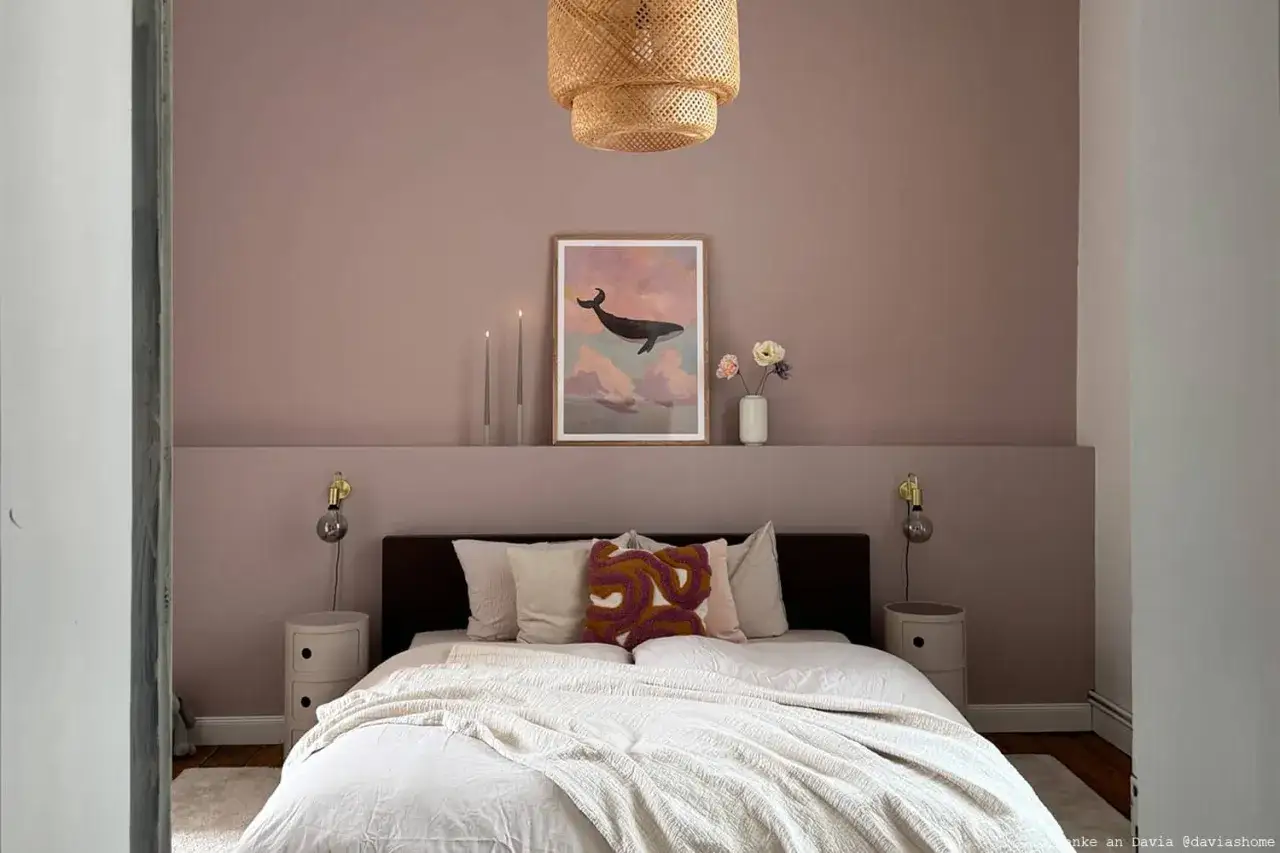 Sanfte Ros&eacute;-**Wandfarbe hinter Bett** mit Walbild, Kerzen und Blumen. Gem&uuml;tliches Schlafzimmer mit Korb-Lampe.
