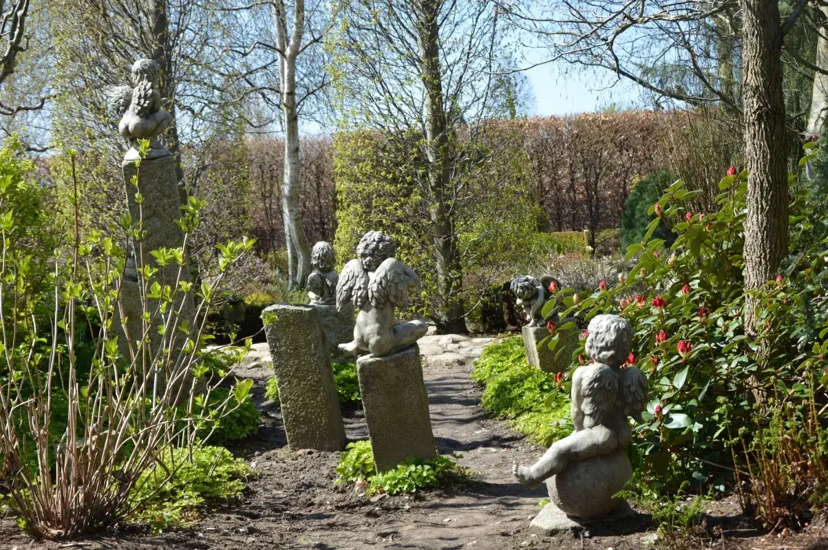 Kamienne aniołki strzegą ścieżki w jednym z najpiękniejszych ogrodów w Polsce. Wiosenna zieleń i kwitnące rododendrony tworzą magiczną atmosferę.