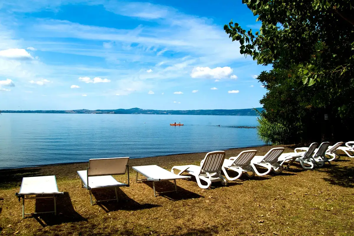 Sdraio e lettini pronti per godersi il **lago di Bolsena balneabile**. In lontananza, un kayak solca le acque calme.