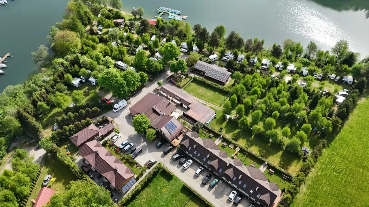 Malowniczy widok na camping w Polańczyku nad jeziorem. Kampery i domki wśród zieleni, z łódkami przy brzegu.