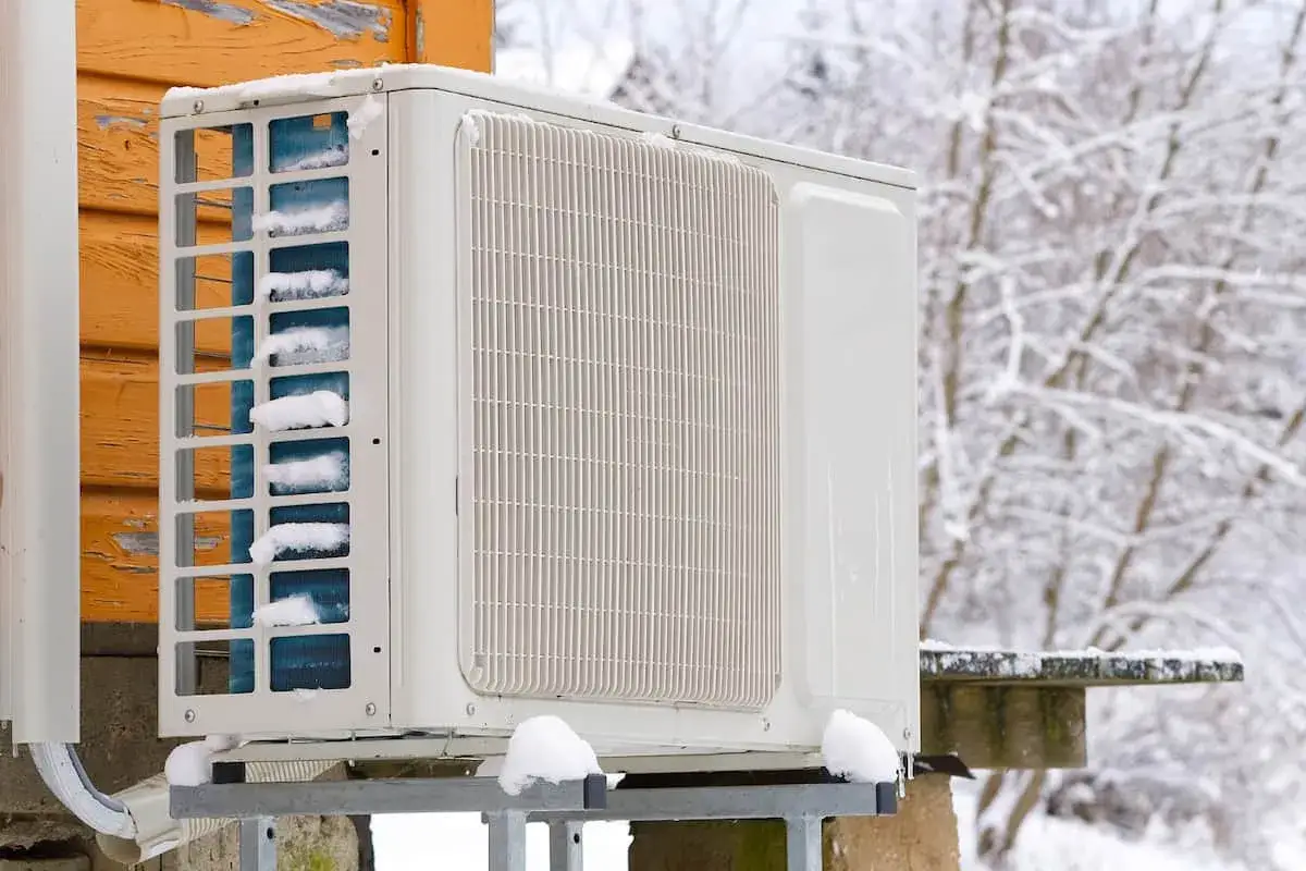 Unité extérieure de climatisation recouverte de neige, témoignant du froid hivernal. La température clim hiver est bien présente.
