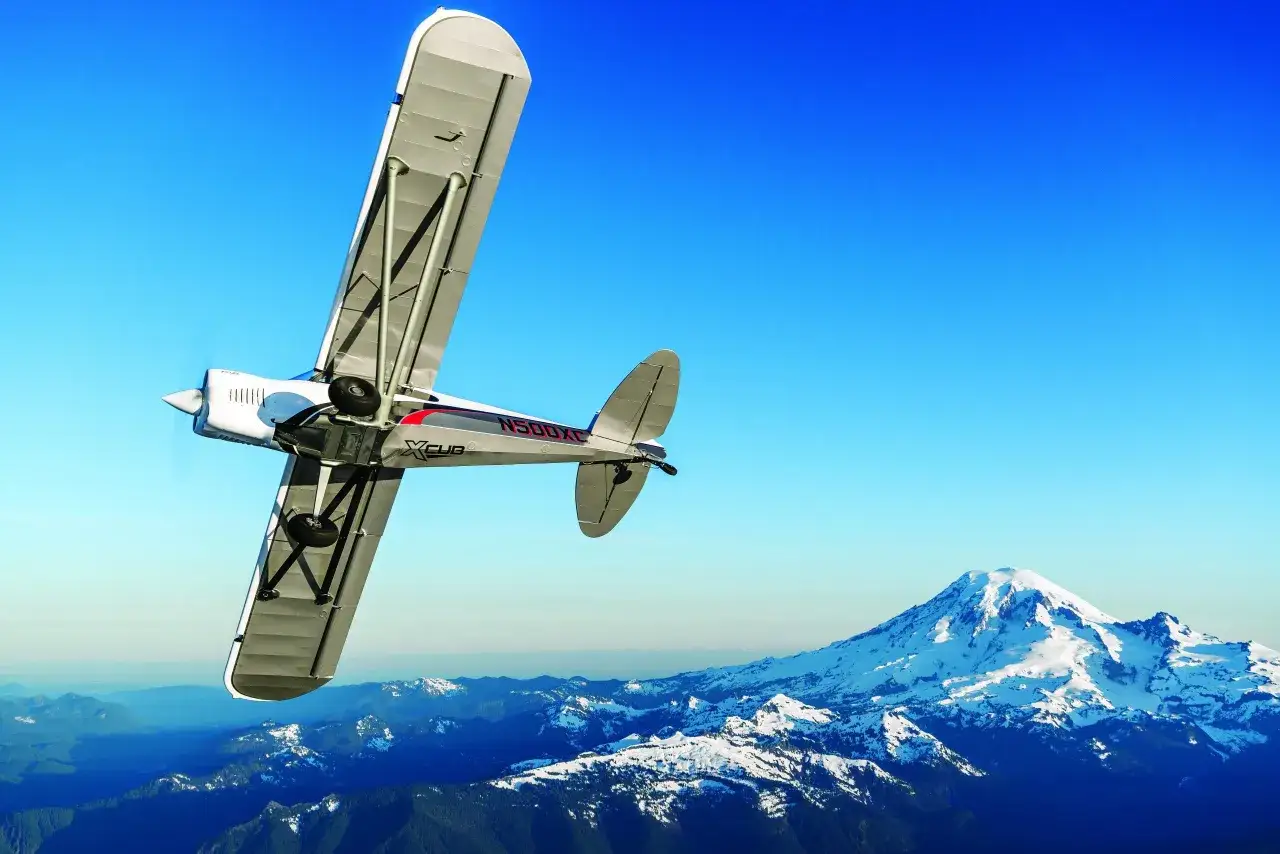 Ein CubCrafters X-Cub fliegt &uuml;ber schneebedeckte Berge.