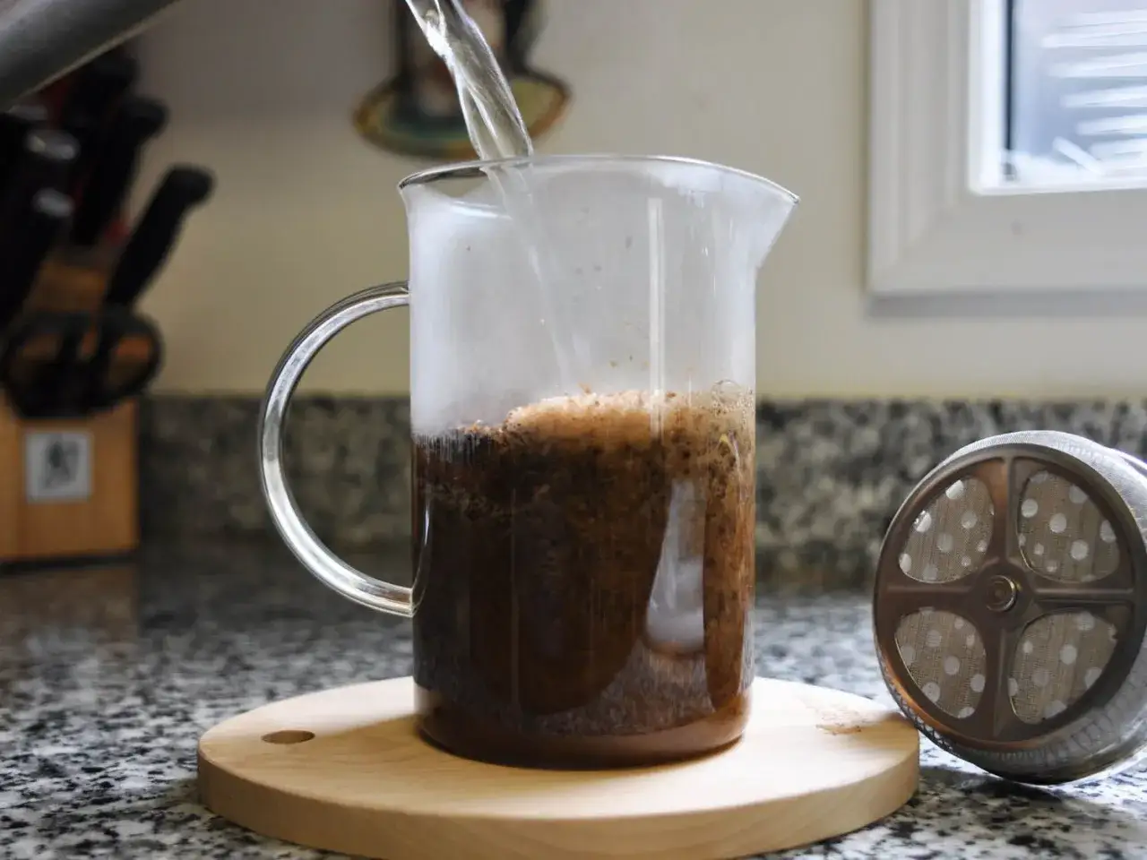 Gorąca woda zalewa zmieloną kawę w szklanym dzbanku. Wkrótce będzie gotowa pyszna french press kawa.