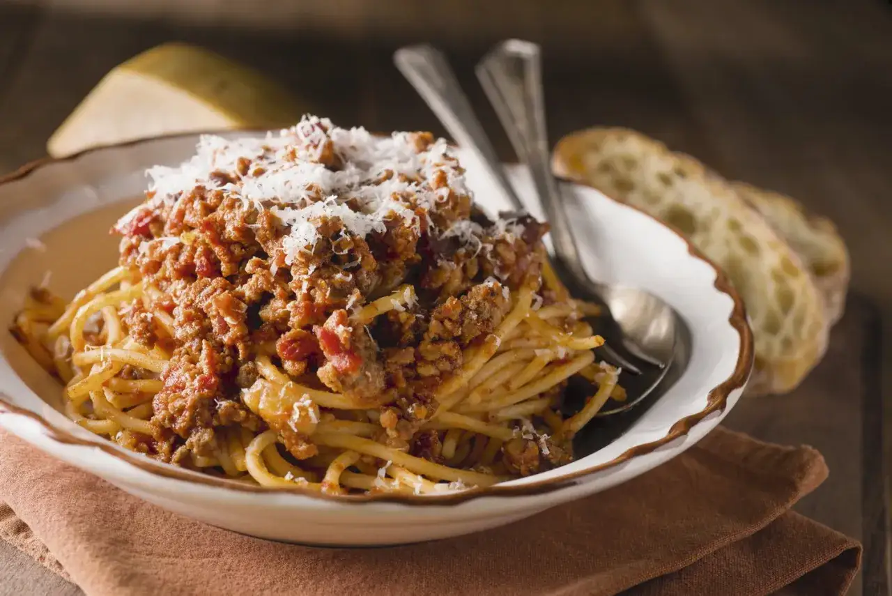 Un plat de spaghetti bolognaise généreux, garni de parmesan râpé, servi avec du pain croustillant.
