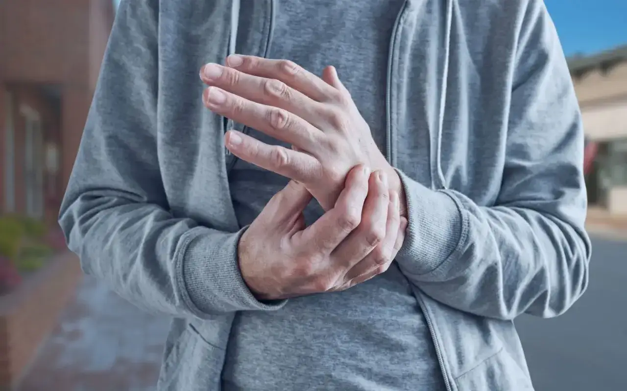 Mężczyzna masuje nadgarstek, odczuwając ostry ból neuropatyczny.