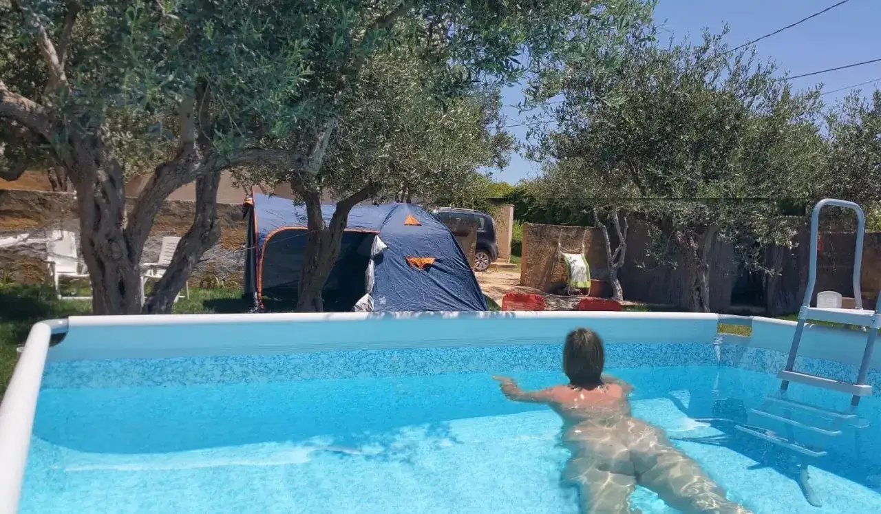 D&eacute;tente dans une piscine lors d'un camping naturiste en Italie. Tentes bleues et oliviers en arri&egrave;re-plan.