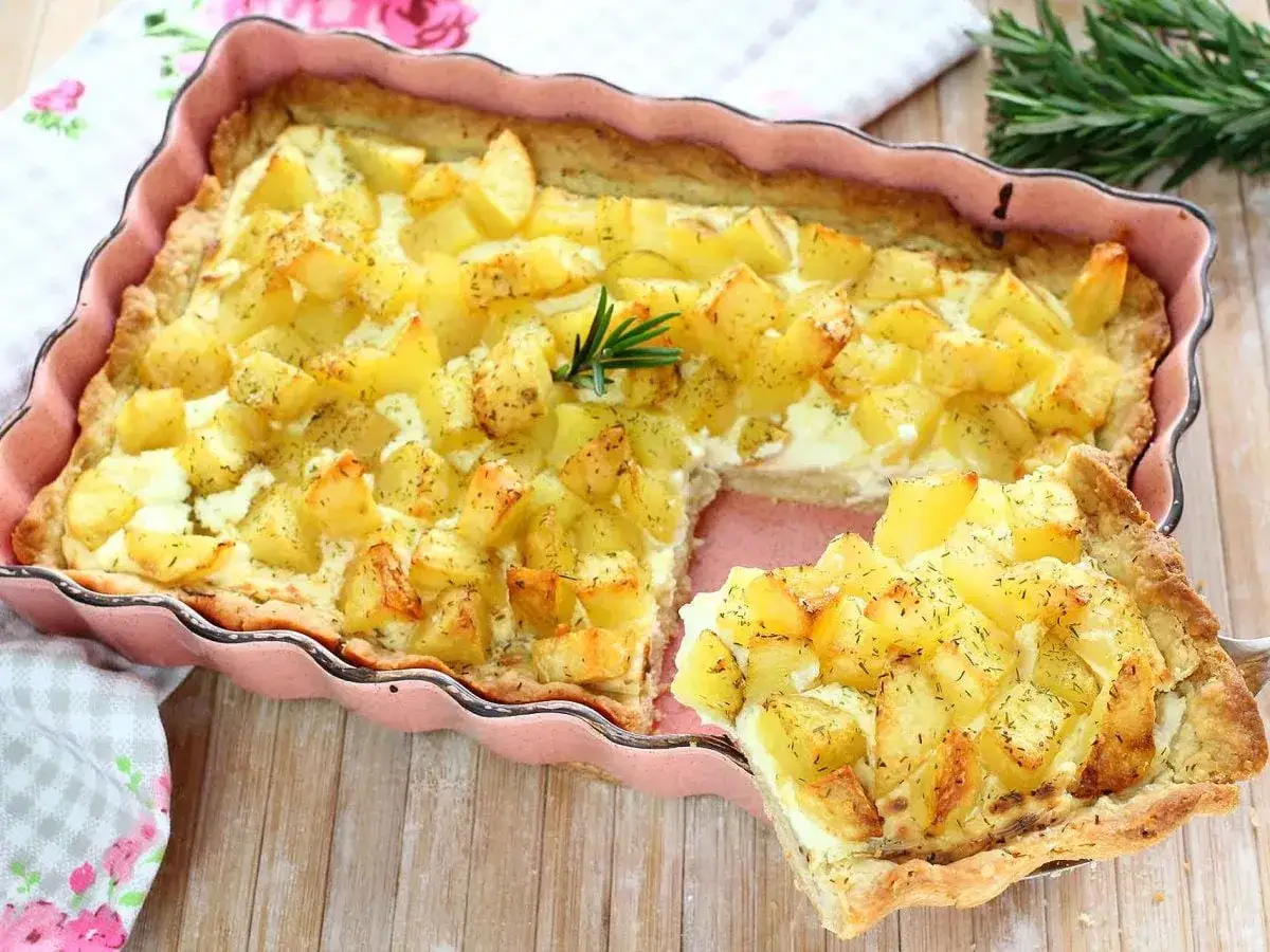Una deliziosa pizza di patate dorate, con erbe aromatiche e formaggio cremoso, servita in una teglia rosa.