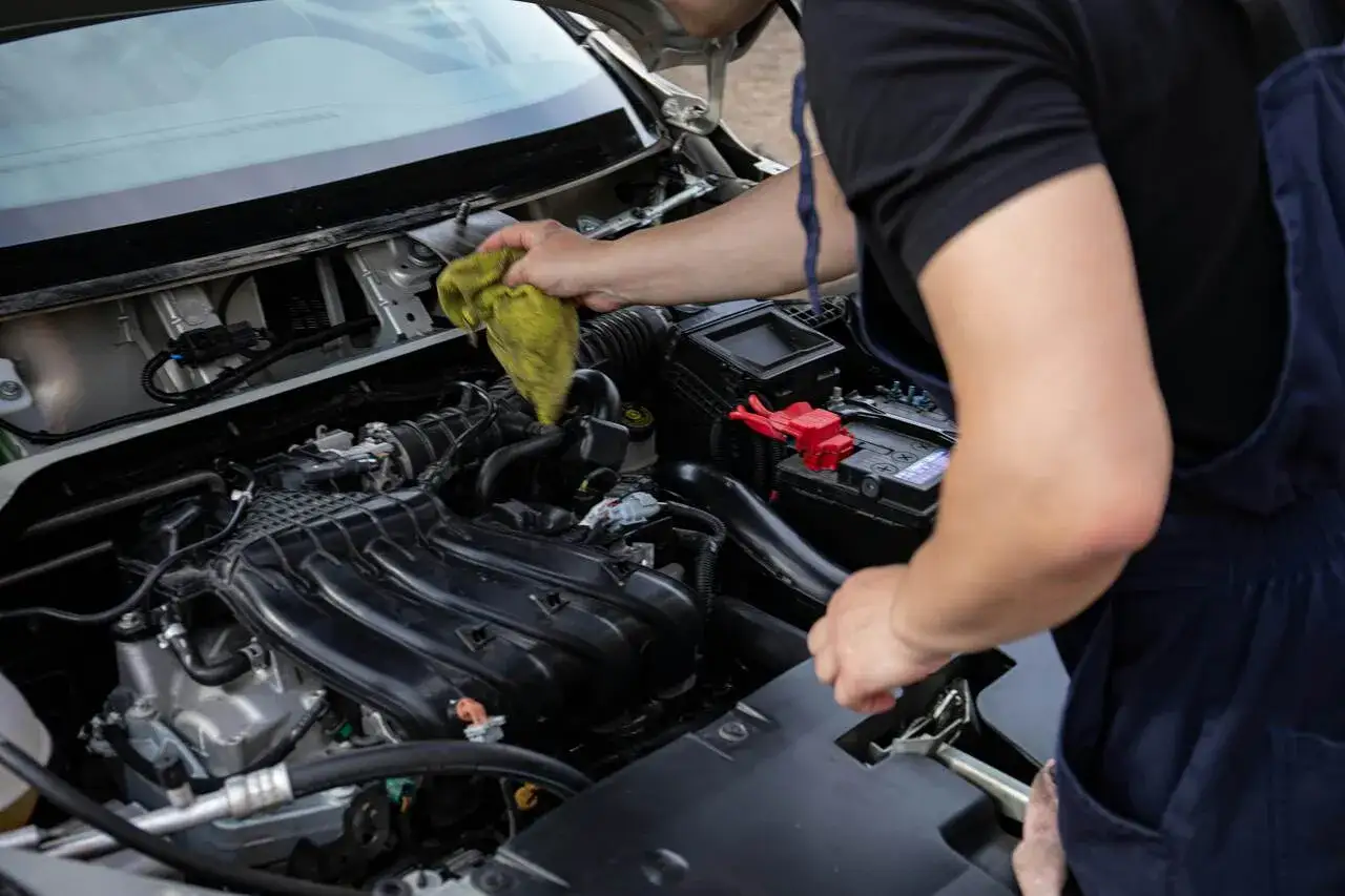 Mechanik czyści przepływomierz w silniku samochodu, używając ż&oacute;łtej ściereczki. Dbałość o detale zapewnia płynną pracę silnika.